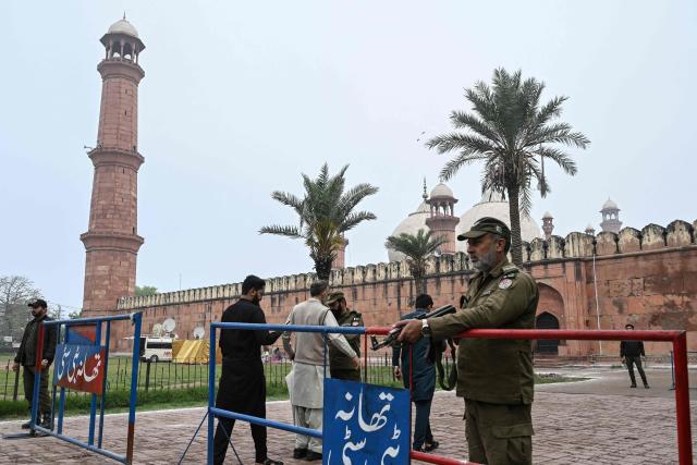 Security personnel stand guard outside the Badshahi Mosque as Muslim devotees arrive to offer Eid al-Fitr prayers, which marks the end of the Islamic holy fasting month of Ramadan in Lahore on March 21, 2026. (Photo by Arif ALI / AFP)