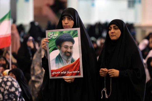 An Iranian woman holds a picture of Iranian supreme leader Ayatollah Mojtaba Khamenei during Eid al-Fitr prayers, marking the end of the Muslim holy month of Ramadan, at the Grand Mosalla mosque in Tehran on March 21, 2026. The Iranian capital has come under near-daily bombardment since a joint US-Israeli attack started the war on February 28, killing top officials, including the Islamic republic's supreme leader. (Photo by AFP) / 