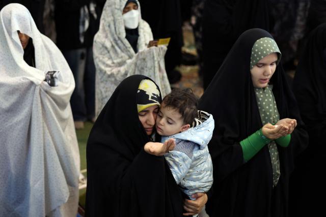 An Iranian Shia woman carrying her child takes part in Eid al-Fitr prayers, marking the end of the Muslim holy month of Ramadan, at the Grand Mosalla mosque in Tehran on March 21, 2026. The Iranian capital has come under near-daily bombardment since a joint US-Israeli attack started the war on February 28, killing top officials, including the Islamic republic's supreme leader. (Photo by AFP) / 