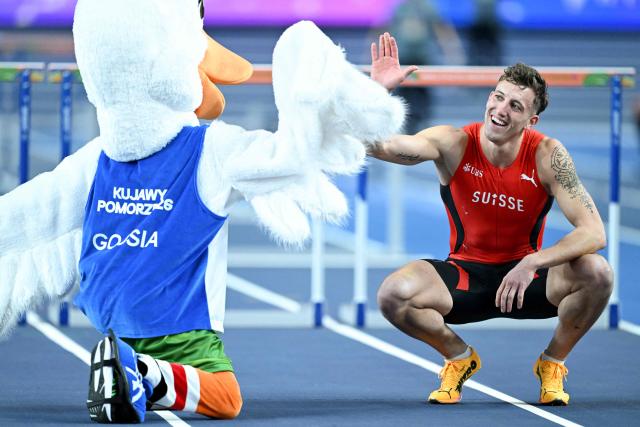 Switzerland's Simon Ehammer reacts with the mascot after finishing first in the men's heptathlon 60 metres hurdles heat 2 during the World Athletics Indoor Championships Kujawy Pomorze 2026 in Torun, Poland on March 21, 2026. (Photo by Kirill KUDRYAVTSEV / AFP)