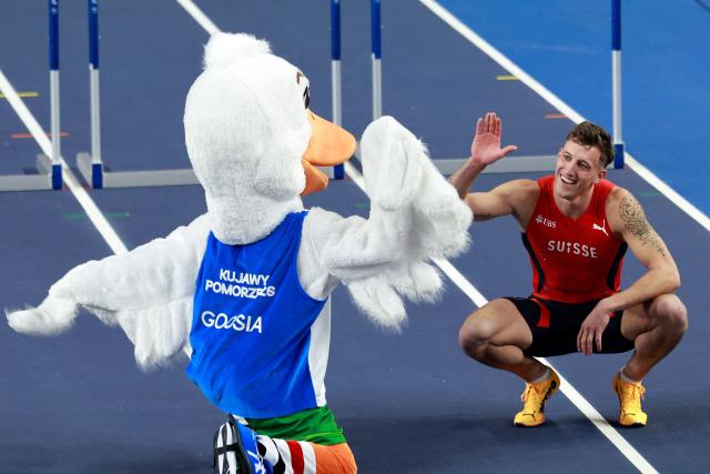 Switzerland's Simon Ehammer reacts with the mascot as he celebrates winning the men's heptathlon 60 metres hurdles heat 2 during the World Athletics Indoor Championships Kujawy Pomorze 2026 in Torun, Poland on March 21, 2026. (Photo by Wojtek RADWANSKI / AFP)