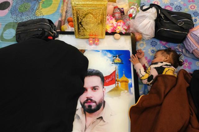 A toddler naps next to a grave at the pro-Iranian armed group Kataeb Hezbollah Cemetery in Iraq's central holy city of Najaf as Shias remember the deceased as well as victims of wars on Eid al-Fitr, marking the end of the fasting month of Ramadan, on March 21, 2026. Iraq has been unwillingly drawn into the regional conflict triggered by the US-Israel attack on its neighbour Iran on February 28. Strikes have targeted Iran-backed groups, which in turn have claimed near-daily attacks on US interests, mostly in Iraq but also across the wider region. (Photo by Qassem al-KAABI / AFP)