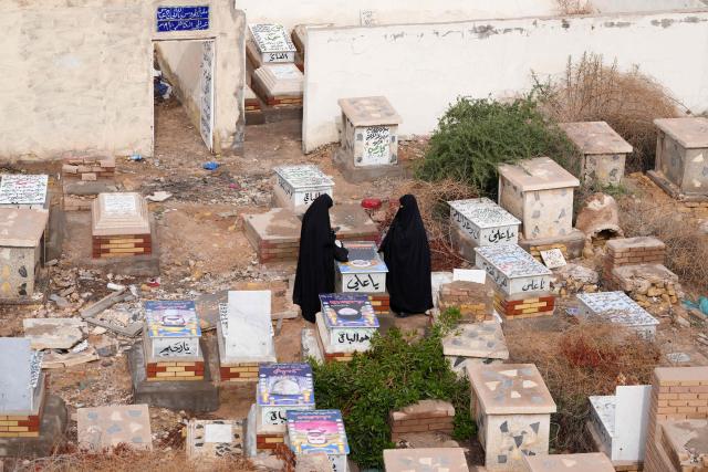Iraqi Shia women visit a grave at Wadi al-Salam Cemetery in Iraq's central holy city of Najaf to remember the deceased as well as victims of wars as they celebrate Eid al-Fitr, marking the end of the fasting month of Ramadan, on March 21, 2026. Iraq has been unwillingly drawn into the regional conflict triggered by the US-Israel attack on its neighbour Iran on February 28. Strikes have targeted Iran-backed groups, which in turn have claimed near-daily attacks on US interests, mostly in Iraq but also across the wider region. (Photo by Qassem al-KAABI / AFP)