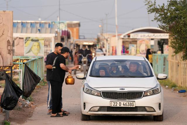 A man distributes tea as Iraqi Shias visit Wadi al-Salam Cemetery in Iraq's central holy city of Najaf to remember the deceased as well as victims of wars as they celebrate Eid al-Fitr, marking the end of the fasting month of Ramadan, on March 21, 2026. Iraq has been unwillingly drawn into the regional conflict triggered by the US-Israel attack on its neighbour Iran on February 28. Strikes have targeted Iran-backed groups, which in turn have claimed near-daily attacks on US interests, mostly in Iraq but also across the wider region. (Photo by Qassem al-KAABI / AFP)