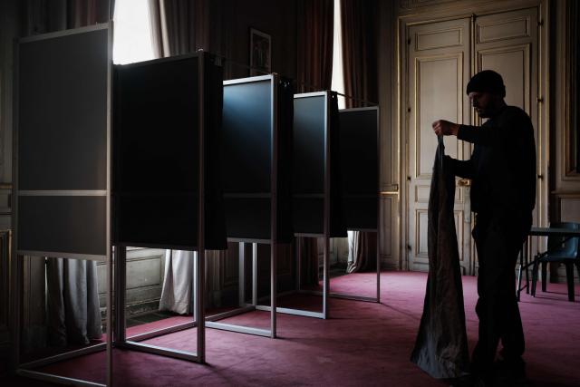 A municipal worker adjusts the curtain of a voting booth in an ornate room of the Bordeaux city hall in Bordeaux, south-western France on March 21, 2026, ahead of France's second round in the 2026 municipal elections. (Photo by Philippe LOPEZ / AFP)