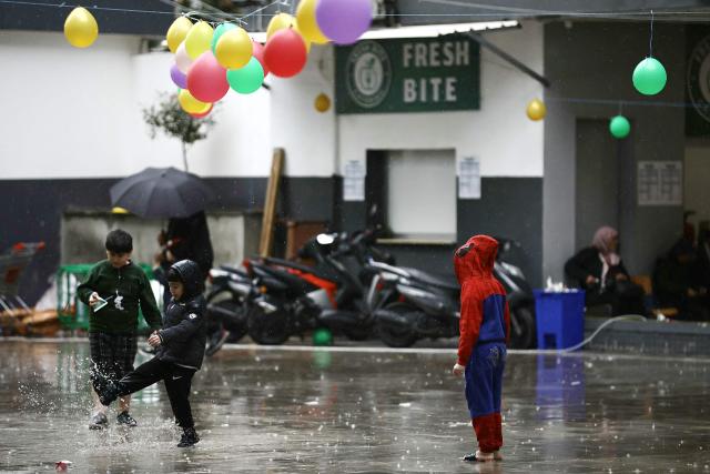 Displaced children from southern Lebanon, including a boy in a Spiderman costume, play in the rain in the playground of a school turned into a shelter in Beirut on March 21, 2026. The Israeli military said it launched a wave of strikes on Beirut targeting the Iran-backed militant group Hezbollah, after urging residents of several areas to evacuate. Lebanon was pulled into the Middle East war when Hezbollah began firing rockets into Israel on March 2 to avenge the killing of Iran's supreme leader Ayatollah Ali Khamenei in US-Israeli strikes. Lebanon's health ministry says the latest war has killed more than 1,000 people in Lebanon and displaced more than one million more. (Photo by ibrahim AMRO / AFP)