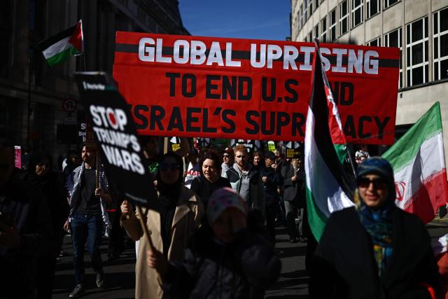 Protesters carry banners and placards during of a protest march in central London on March 21, 2026, calling for the bombing of Iran to stop. Britain has authorised the United States to use its bases to strike Iranian sites threatening the Strait of Hormuz shipping lane, the government said Friday. (Photo by Henry NICHOLLS / AFP)