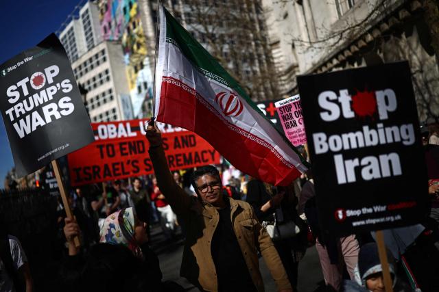 Protesters carry Iranian flags, banners and placards during of a protest march in central London on March 21, 2026, calling for the bombing of Iran to stop. Britain has authorised the United States to use its bases to strike Iranian sites threatening the Strait of Hormuz shipping lane, the government said Friday. (Photo by Henry NICHOLLS / AFP)
