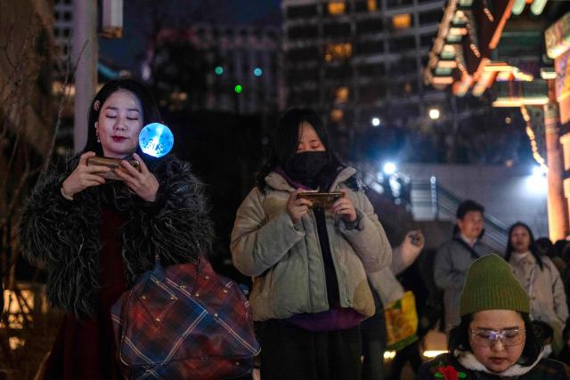 Fans watch the comeback concert of K-pop boy group BTS on their mobile phones at the venue in Seoul on March 21, 2026. South Korean megastars BTS reunited on March 21 for their first show in nearly four years, blowing away enormous crowds in Seoul for a K-pop extravaganza livestreamed to millions more worldwide. (Photo by Roland DE COURSON / AFP)