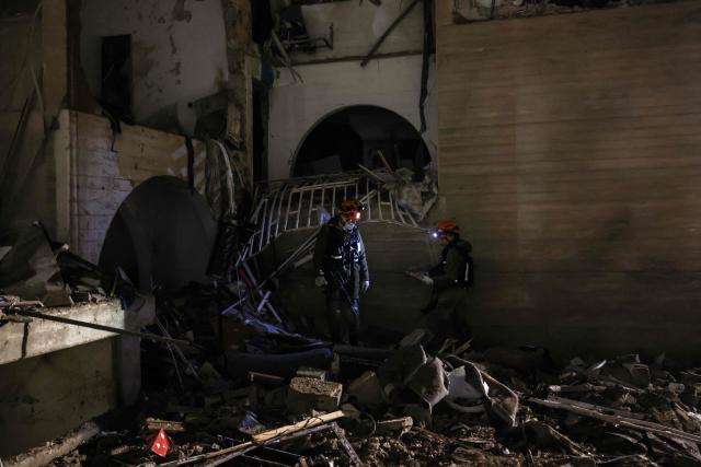 TOPSHOT - First responders inspect the site of an Iranian missile strike in Arad early on March 22, 2026. Iranian missile strikes on two southern Israeli towns wounded more than 100 people on March 21, medics said, after Israeli air defence systems failed to intercept the projectiles. (Photo by Ilia YEFIMOVICH / AFP) / 