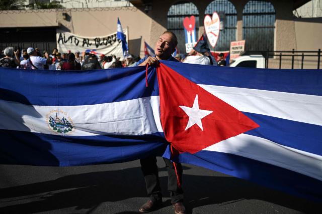A man holds Salvadorian and Cuban flags during a demonstration in solidarity with Cuba and against the US embargo, under the slogan “Cuba is not a threat,” outside the Cuban embassy in San Salvador on March 21, 2026. (Photo by Marvin RECINOS / AFP)