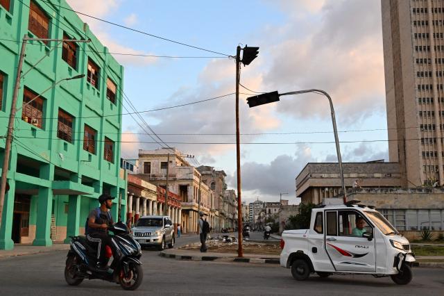 People transit on a street with traffic lights without power during a nation wide blackout in Havana on March 21, 2026. A power outage struck the entire island of Cuba on March 21, 2026, the energy ministry said, in the second nationwide blackout in less than a week as its grid struggles under a US oil blockade. (Photo by Yamil LAGE / AFP)