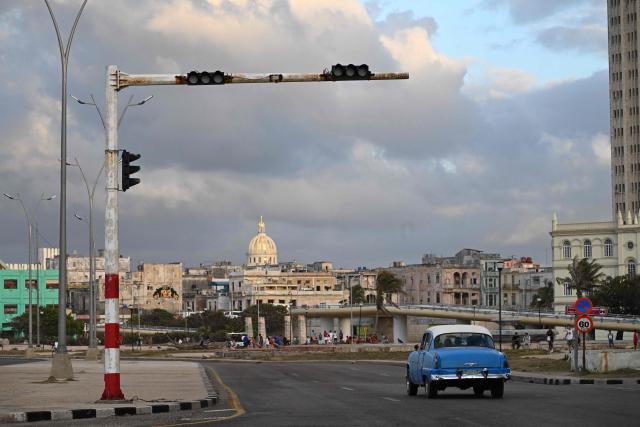 People transit on a street with traffic lights without power during a nation wide blackout in Havana on March 21, 2026. A power outage struck the entire island of Cuba on March 21, 2026, the energy ministry said, in the second nationwide blackout in less than a week as its grid struggles under a US oil blockade. (Photo by Yamil LAGE / AFP)