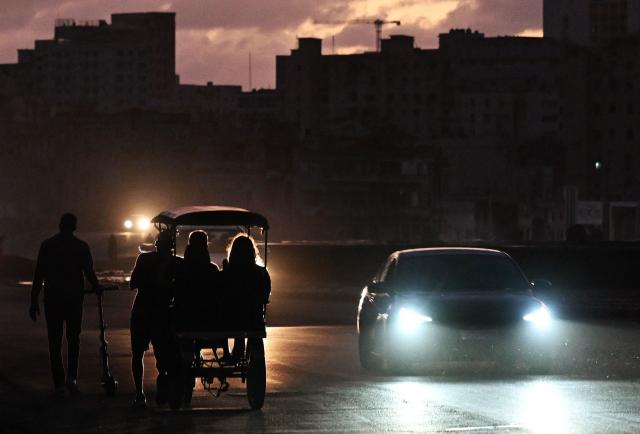 People transit on a street without power during a nation wide blackout in Havana on March 21, 2026. A power outage struck the entire island of Cuba on March 21, 2026, the energy ministry said, in the second nationwide blackout in less than a week as its grid struggles under a US oil blockade. (Photo by Yamil LAGE / AFP)