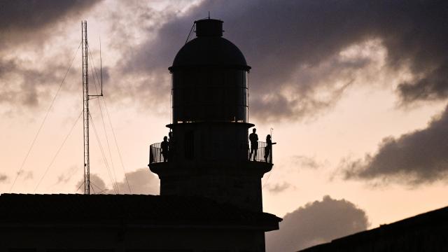 People stand on a balcony during a nation wide blackout in Havana on March 21, 2026. A power outage struck the entire island of Cuba on March 21, 2026, the energy ministry said, in the second nationwide blackout in less than a week as its grid struggles under a US oil blockade. (Photo by ADALBERTO ROQUE / AFP)