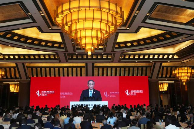 Chinese Premier Li Qiang is seen on a big screen live broadcasting his speech at the opening of the China Development Forum 2026 held at the Diaoyutai State Guesthouse in Beijing on March 22, 2026. (Photo by Ng Han Guan / POOL / AFP)