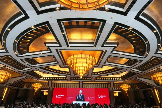 Apple CEO Tim Cook is seen on a big screen live broadcasting his speech at the opening of the China Development Forum 2026 held at the Diaoyutai State Guesthouse in Beijing on March 22, 2026. (Photo by Ng Han Guan / POOL / AFP)