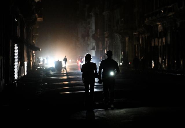 people walk on a street without power during a nation wide blackout in Havana on March 21, 2026. A power outage struck the entire island of Cuba on March 21, 2026, the energy ministry said, in the second nationwide blackout in less than a week as its grid struggles under a US oil blockade. (Photo by Yamil LAGE / AFP)