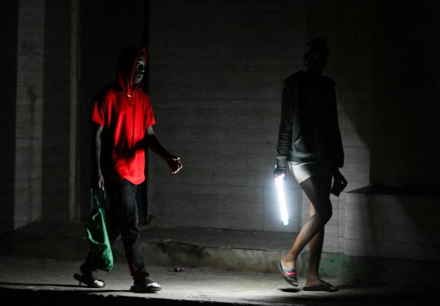 people walk on a street without power during a nation wide blackout in Havana on March 21, 2026. A power outage struck the entire island of Cuba on March 21, 2026, the energy ministry said, in the second nationwide blackout in less than a week as its grid struggles under a US oil blockade. (Photo by Yamil LAGE / AFP)