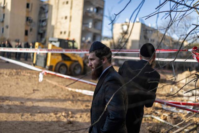 Israeli Orthodox Jews inspect the site of an Iranian missile strike in Arad on March 22, 2026. Iranian missile strikes on two southern Israeli towns wounded more than 100 people on March 21, medics said, after Israeli air defence systems failed to intercept the projectiles. (Photo by Ilia YEFIMOVICH / AFP) / 