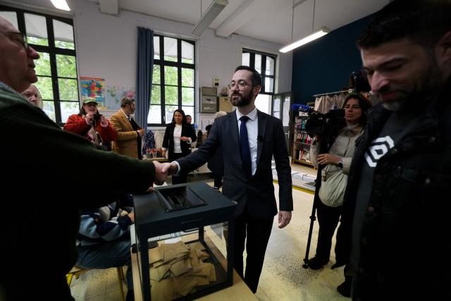 Roubaix' Left-wing La France Insoumise (LFI, Unbowed France) mayoral candidate David Guiraud (C) shakes hands with a local resident as he prepares to cast his vote during the second round of France's 2026 municipal elections in Roubaix, northern France on March 22, 2026. (Photo by Francois LO PRESTI / AFP)