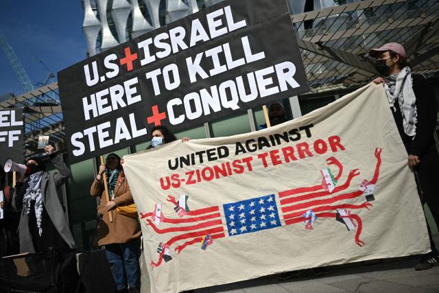 Protesters hold banners at a mass unity protest set to highlight opposition to the conflict in Middle East and restrictions against Cuba being imposed by the US, outside the US Embassy in central London on March 22, 2026. The protest is one of dozens of other protests taking place across the world outside US embassies. (Photo by JUSTIN TALLIS / AFP)