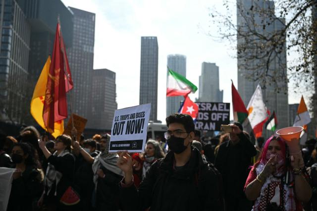 Protesters hold placards and wave flags at a mass unity protest set to highlight opposition to the conflict in Middle East and restrictions against Cuba being imposed by the US, in central London on March 22, 2026. The protest is one of dozens of other protests taking place across the world outside US embassies. (Photo by JUSTIN TALLIS / AFP)