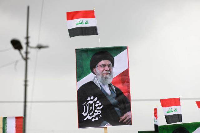 The Iraqi flag and an image of the assassinated Iranian supreme leader Ayatollah Ali Khamenei, are held up as Iraqis rally in support of neighbouring Iran, in the al-Aamil district of Baghdad on March 22, 2026. On February 28, Israel and the United States launched strikes on Iran killing its supreme leader and triggering a war that spread across the Middle East and unleashed chaos across global markets and sent oil prices soaring. (Photo by Murtaja LATEEF / AFP) / 