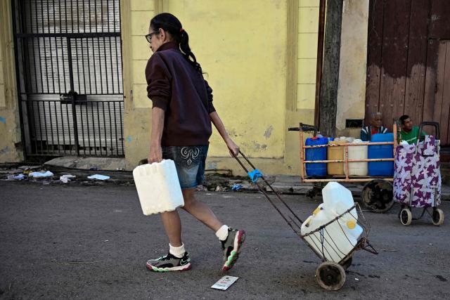 A woman pushes her cart after filling her water containers in Havana during a national blackout on March 22, 2026. Cuban authorities scrambled on March 22 to restore power to the island after the second nationwide blackout in less than a week, as the grid struggles due to an aging infrastructure and a US oil blockade. (Photo by YAMIL LAGE / AFP)