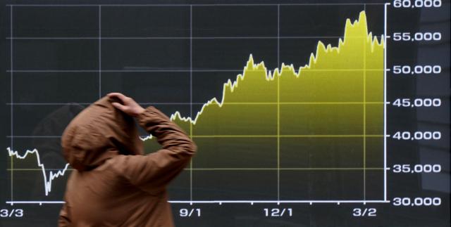 A passerby looks at a graph depicting stock market trends on the Tokyo Stock Exchange along a street in Tokyo on March 23, 2026. (Photo by Kazuhiro NOGI / AFP)