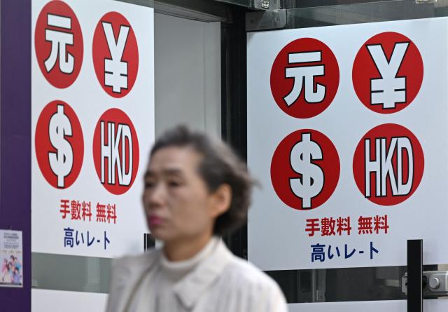 A pedestrian walks past a money exchange sign at a shopping district in Seoul on March 23, 2026. South Korea's won dropped to its weakest level against the US dollar in 17 years in early trading on March 23, amid market volatility sparked by the Iran war. (Photo by Jung Yeon-je / AFP)