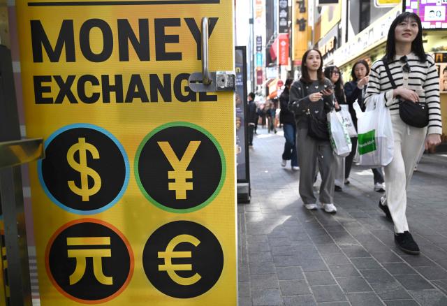 Pedestrians walk past a money exchange sign at a shopping district in Seoul on March 23, 2026. South Korea's won dropped to its weakest level against the US dollar in 17 years in early trading on March 23, amid market volatility sparked by the Iran war. (Photo by Jung Yeon-je / AFP)