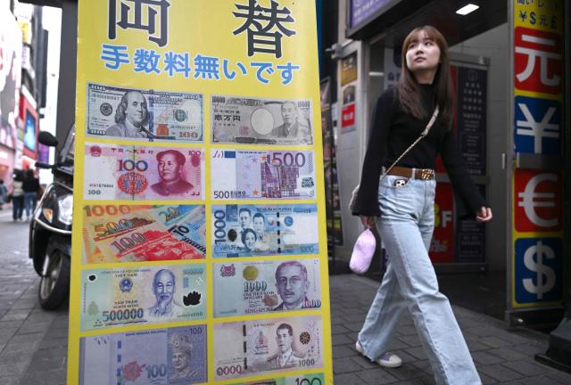 A pedestrian walks past a money exchange sign at a shopping district in Seoul on March 23, 2026. South Korea's won dropped to its weakest level against the US dollar in 17 years in early trading on March 23, amid market volatility sparked by the Iran war. (Photo by Jung Yeon-je / AFP)