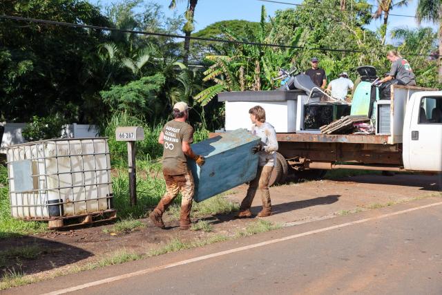 Residents and volunteers move debris off the road after the Kona Low storm flood devastated the Otake Camp community in Waialua, Hawaii, on March 22, 2026. Severe rains have battered the region over the weekend prompting officials to order evacuations. (Photo by Marco GARCIA / AFP)