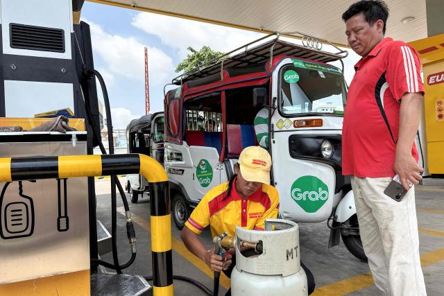 An employee (C) pumps liquefied petroleum gas (LPG) into a customer's container at a fuel station in Phnom Penh on March 23, 2026. A major energy supplier in Cambodia has said it will halt sales of liquefied petroleum gas from the start of next month due to supply disruptions resulting from the Middle East war. (Photo by TANG CHHIN Sothy / AFP)