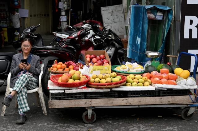 A street fruit vendor sits with her phone while waiting for customers in Hanoi on March 23, 2026. (Photo by Nhac NGUYEN / AFP)