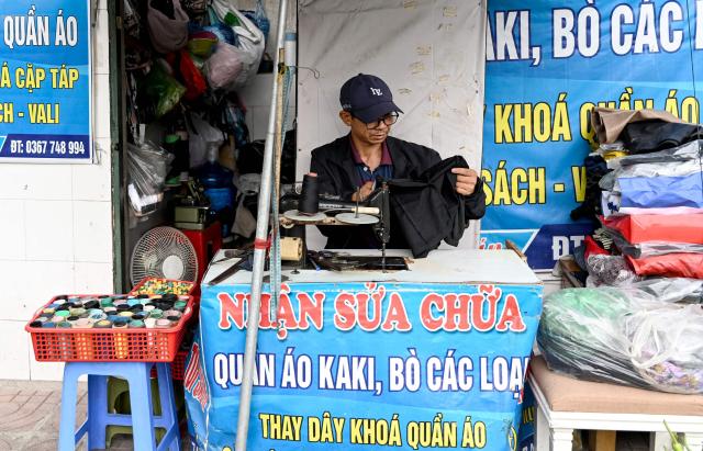 A clothes mender works on a sidewalk in Hanoi on March 23, 2026. (Photo by Nhac NGUYEN / AFP)