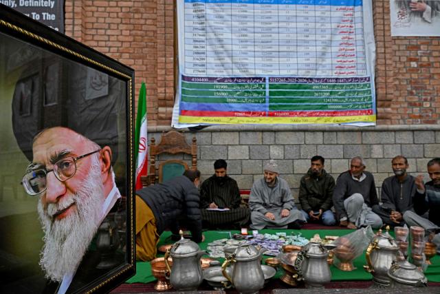 Kashmiri Muslims sit next to a portait of Iran's late supreme leader Ayatollah Ali Khamenei as they conduct a donation drive for war-stricken Iran, collecting cash, gold, and other contributions amid the Middle East conflict, on the outskirts of Srinagar on March 23, 2026. (Photo by Tauseef MUSTAFA / AFP)
