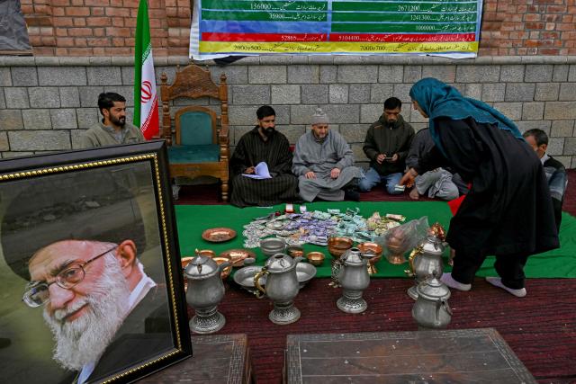 Kashmiri Muslims sit next to a portait of Iran's late supreme leader Ayatollah Ali Khamenei as they conduct a donation drive for war-stricken Iran, collecting cash, gold, and other contributions amid the Middle East conflict, on the outskirts of Srinagar on March 23, 2026. (Photo by Tauseef MUSTAFA / AFP)