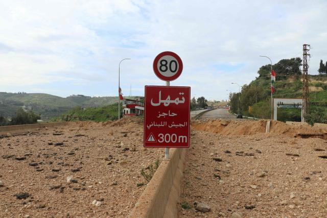 A traffic sign reading “Slow Lebanese Army Checkpoint” stands beside a crater the day after an Israeli airstrike targeted the Qasmiyeh Bridge, located on a main highway linking villages in the Tyre district with others farther north, after Israel said the bridge was being used by Hezbollah, in southern Lebanon on March 23, 2026. The Lebanese president on March 22, 2026, slammed Israeli strikes on bridges and other infrastructure in the country's south, calling such attacks a "prelude to a ground invasion". Lebanon was drawn into the Middle East war on March 2, when pro-Iran Hezbollah launched rockets towards Israel in response to US-Israeli strikes that killed Iranian supreme leader on February 28, 2026. (Photo by Kawnat HAJU / AFP) / 
