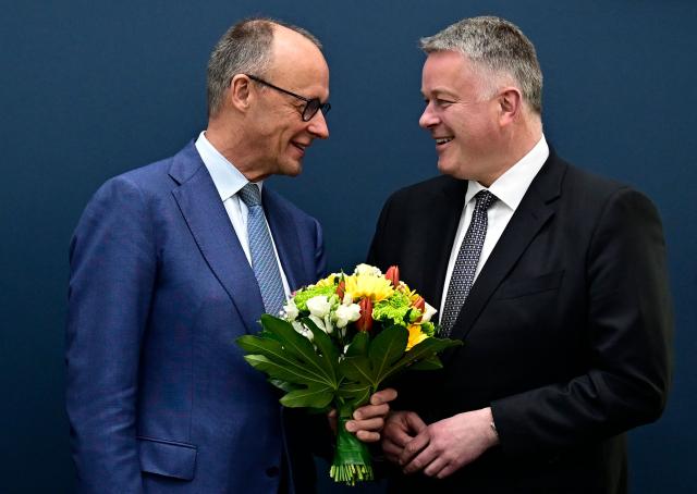 German Chancellor Friedrich Merz gives a bouquet of flowers to Gordon Schnieder, the conservative CDU party's top candidate for state elections in the southwestern state of Rhineland-Palatinate, on March 23, 2026, one day after the vote, at the CDU's headquarters in Berlin. German Chancellor Friedrich Merz's conservatives ousted the centre-left Social Democratic Party in the closely watched state election in which the far right also made big gains, according to exit polls. (Photo by Tobias SCHWARZ / AFP)