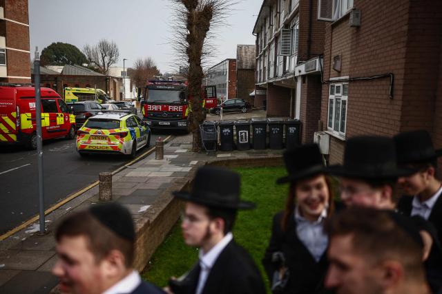 Local residents gather in the Golders Green neighbourhood of north London on March 23, 2026, after volunteer ambulances (back L) run by a Jewish organisation were set on fire overnight. Britain's Prime Minister Keir Starmer on March 23 condemned "a deeply shocking antisemitic arson attack" on volunteer ambulances run by a Jewish organisation in London. (Photo by Henry Nicholls / AFP)