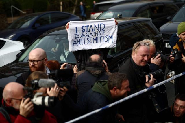 A woman holds up a banner reading "I stand against anti semitism" as members of the media gather in the Golders Green neighbourhood of north London on March 23, 2026, after volunteer ambulances run by a Jewish organisation were set on fire overnight. Britain's Prime Minister Keir Starmer on March 23 condemned "a deeply shocking antisemitic arson attack" on volunteer ambulances run by a Jewish organisation in London. (Photo by Henry NICHOLLS / AFP)