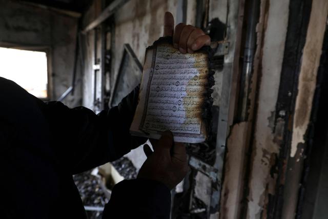 A Palestinian man holds up a burnt page of the koran, Islam's holy book, as he inspects a burnt out home following a reported attack by Israeli settlers in the village of Deir al-Hatab, east of the city of Nablus, in the Israeli-occupied West Bank on March 23, 2026. Palestinian residents said on March 22, 2026, that Israeli settlers torched buildings and cars in attacks on several villages in the occupied West Bank, with Israel's army condemning "violence of any kind" after the fact.  Violence in the Palestinian West Bank, which Israel has occupied since 1967, has soared since the Hamas attack on Israel triggered the Gaza war in October 2023. (Photo by JAAFAR ASHTIYEH / AFP)
