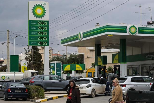 People pass by in front of a gas station in Athens on March 23, 2026. Greek Prime Minister Kyriakos Mitsotakis on March 23, 2026 announced a raft of additional measures to mitigate the energy cost of the Middle East war. (Photo by Aris MESSINIS / AFP)