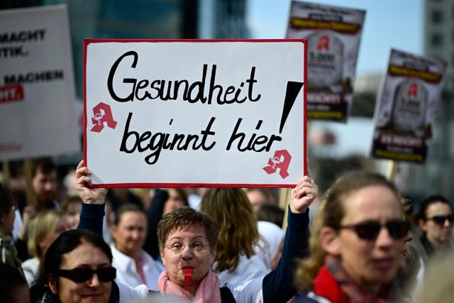 A woman holds up a poster reading "Health is starting here!" as protesters take part in a demonstration organised by the Federal Union of German Pharmacists' Associations (ABDA, Bundesvereinigung Deutscher Apothekerverbaende) on March 23, 2026 in Berlin. Pharmacists across the country staged a protest, closing their pharmacies and holding rallies to demand a pay rise. (Photo by Tobias SCHWARZ / AFP)