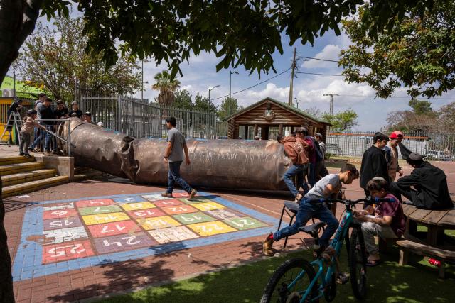 Children play with an Iranian missile remnant that fell in a school courtyard in the Israeli settlement of Peduel, in the occupied West Bank on March 23, 2026. Iran has been firing barrages of missiles at Israel in response to the bombing campaign by Israel and the United States that started on February 28, following the killing of the country's supreme leader. (Photo by Maya Levin / AFP) / 
