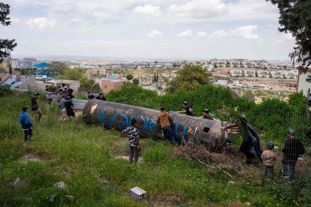 Children move part of an Iranian missile remnant that fell in a school courtyard in the Israeli settlement of Peduel, in the occupied West Bank on March 23, 2026. Iran has been firing barrages of missiles at Israel in response to the bombing campaign by Israel and the United States that started on February 28, following the killing of the country's supreme leader. (Photo by Maya Levin / AFP) / 