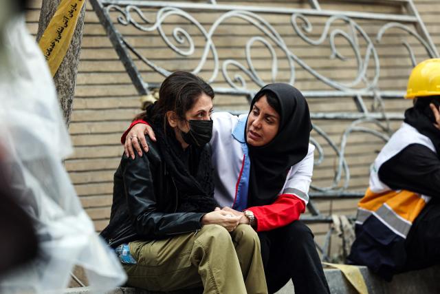 A member of the Iranian Red Crescent comforts a resident of a destroyed apartment block in northern Tehran on March 23, 2026. A series of strong explosions were heard in the Iranian capital on March 23, an AFP journalist said, as the war with the United States and Israel raged for its fourth week. On February 28, Israel and the United States launched strikes on Iran killing its supreme leader and triggering a war that spread across the Middle East and unleashed chaos across global markets and sent oil prices soaring. (Photo by AFP) / 