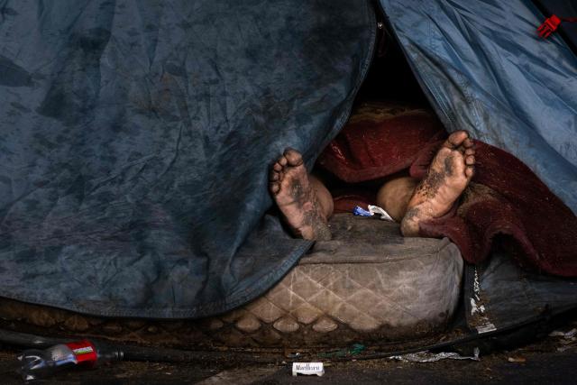 A homeless man sleeps in his tent pitched on a sidewalk in Paris on March 21, 2026. (Photo by JOEL SAGET / AFP)